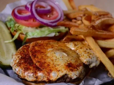 A burger with fried eggs, fries, and pickle spear in a basket.