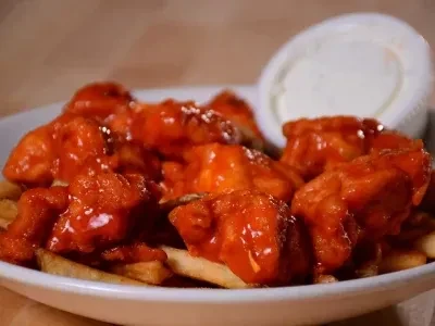 Red-sauced chicken pieces on french fries, with a side dipping sauce.