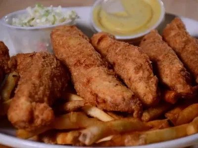 Fried tenders, french fries, coleslaw, and dipping sauce on a plate.
