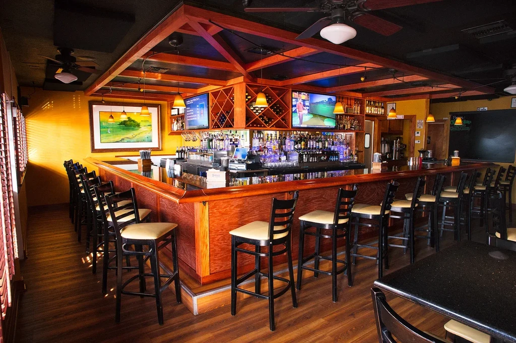 L-shaped wooden bar with stools, TVs, and wine racks in restaurant.