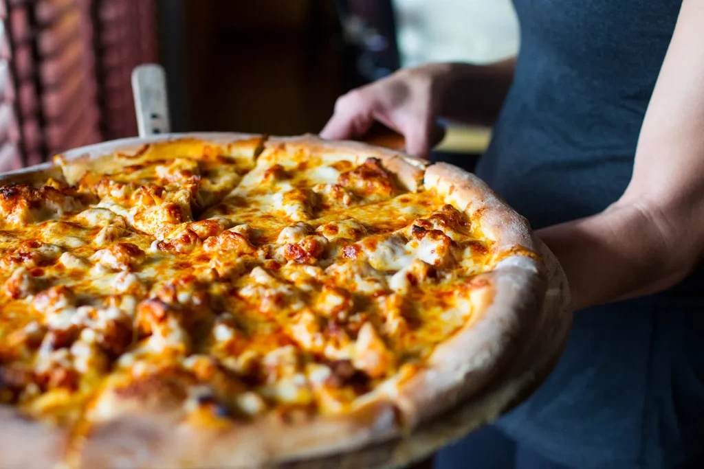 Sliced pizza with melted cheese, meat, and sauce, held by hands.