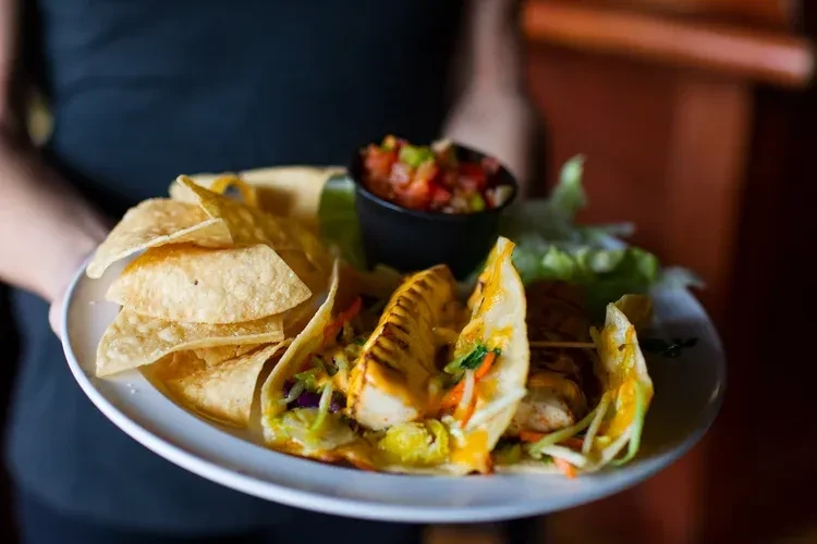 Three grilled fish tacos, chips, and salsa on white plate.