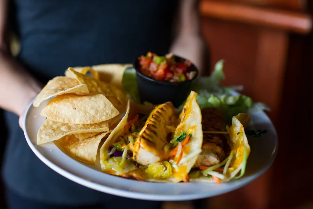 Person holds plate with three tacos, chips, and salsa.