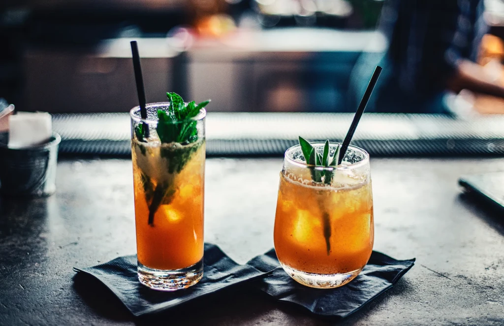 Two amber-orange cocktails with ice and herbs on a dark bar.