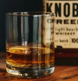 Knob Creek bourbon in a glass with ice on wood.