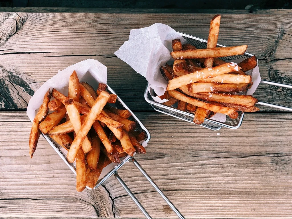 Two servings of salted hand-cut fries in baskets on a wooden table.