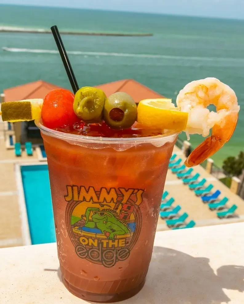 Garnished Bloody Mary with shrimp, lemon, and gherkin by a pool.