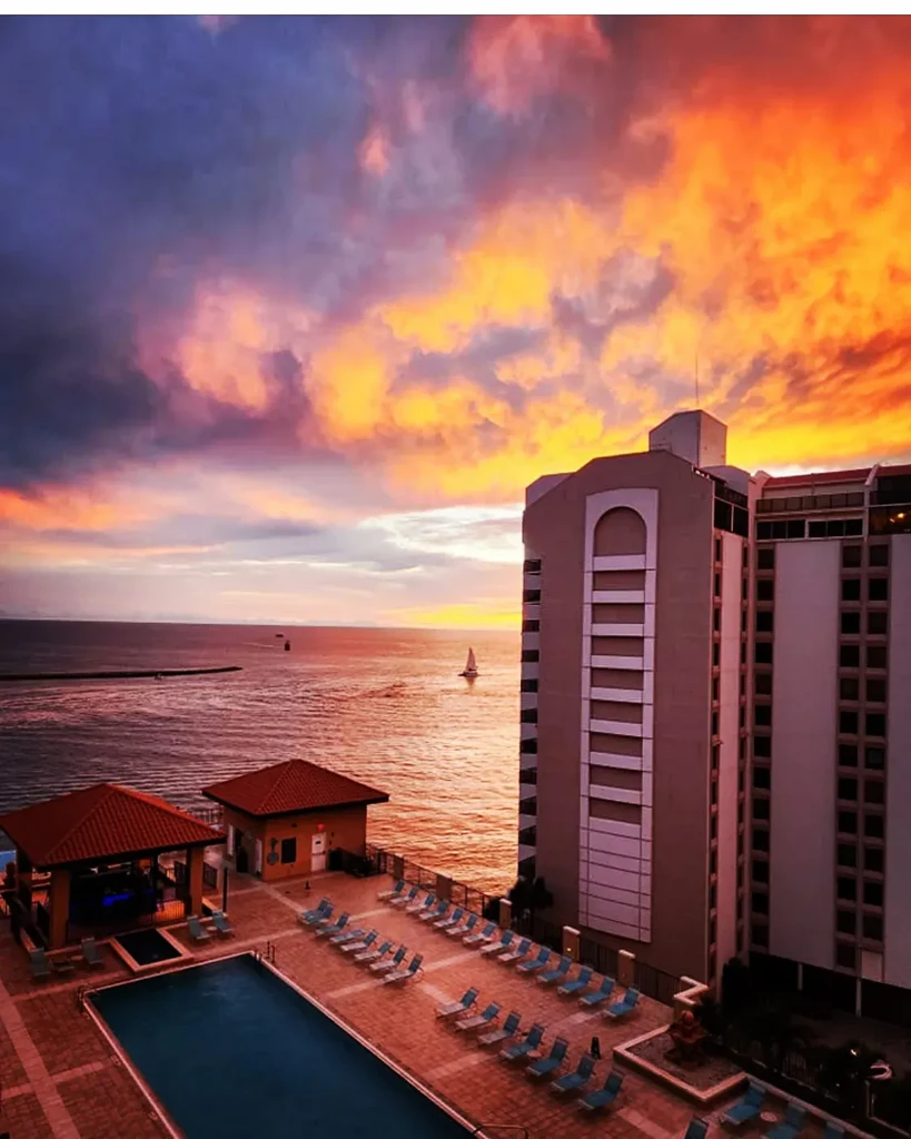 High-angle view of oceanfront resort with pool at vibrant sunset.