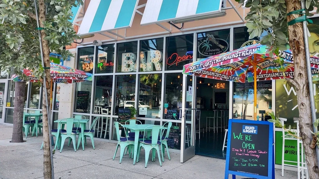 Exterior of a bar with outdoor seating, striped awning, and 'WE'RE OPEN' sign.