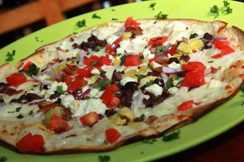 Flatbread pizza with tomatoes, olives, cheese on lime-green plate.