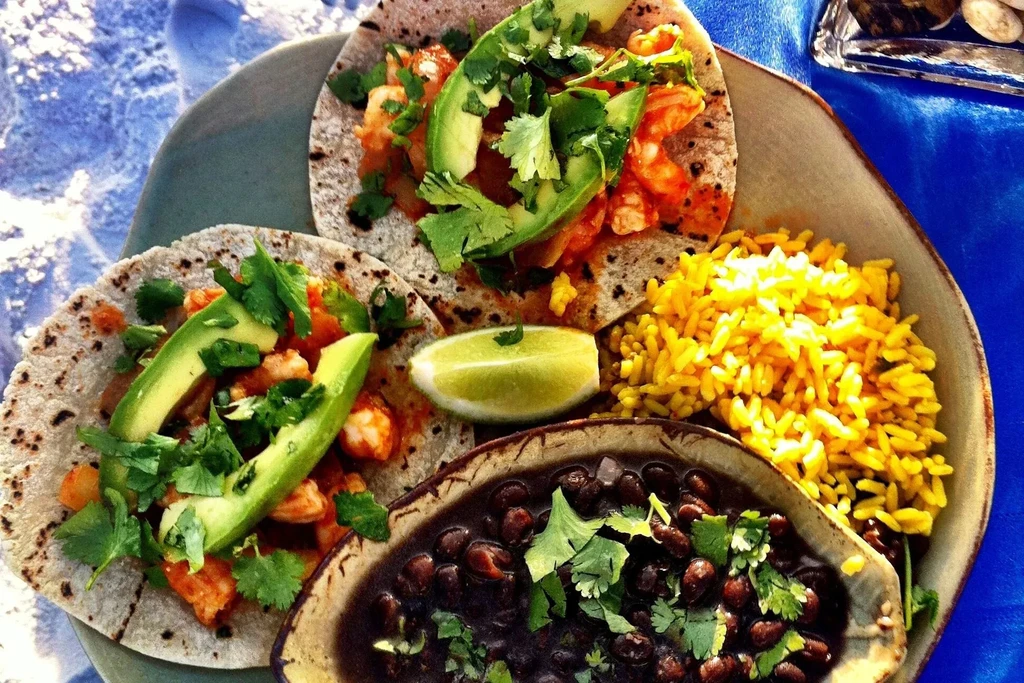 Colorful shrimp tacos with avocado, cilantro, rice, black beans, lime.