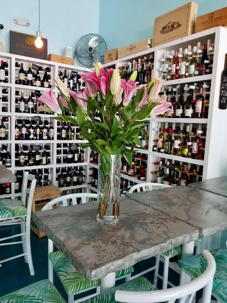 Interior of a wine bar with lilies, wine bottles, and palm-leaf chairs.