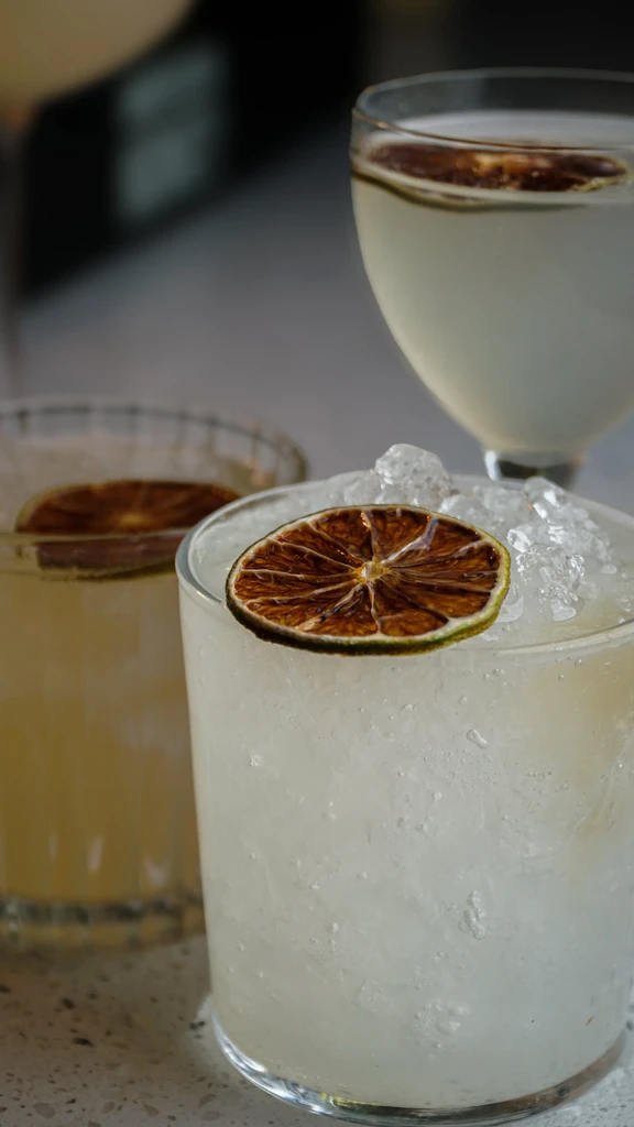 Three drinks with dried citrus garnishes on a light countertop.