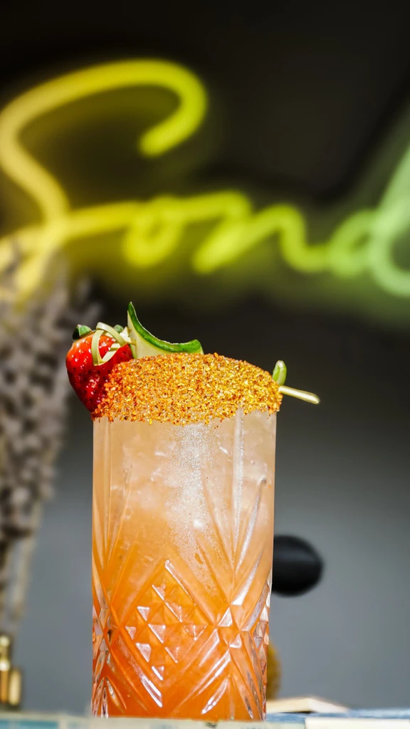 Cold cocktail with spicy rim, strawberry, cucumber, and neon sign.