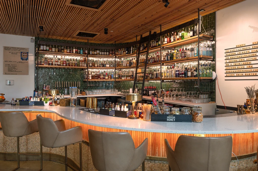 Empty modern bar with curved counter, illuminated liquor, green tiles.