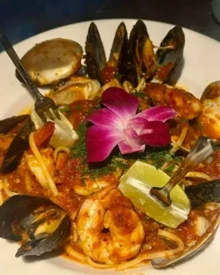Seafood pasta with mussels, shrimp, clams, an orchid, and lime.