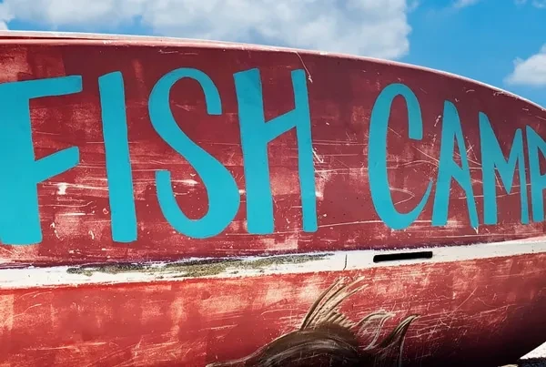 Close-up of weathered red boat reading 'FISH CAMP' against blue sky.