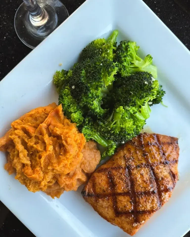 Grilled salmon, orange sweet potatoes, and green broccoli on a white plate.