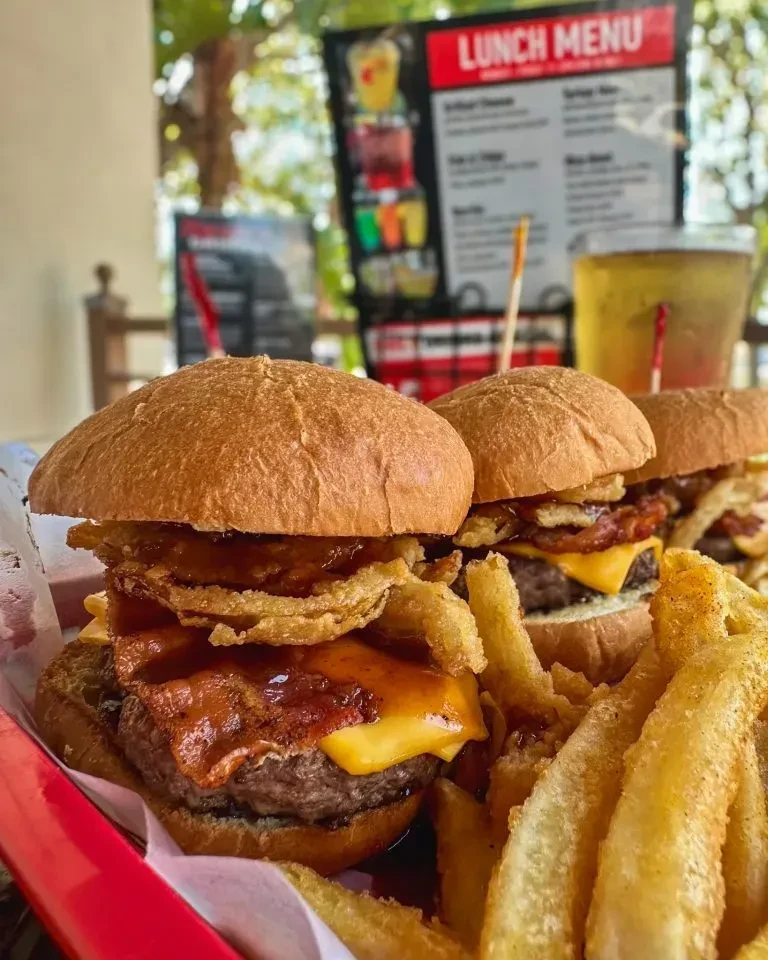 Three sliders topped with cheese, bacon, onion rings, and french fries.