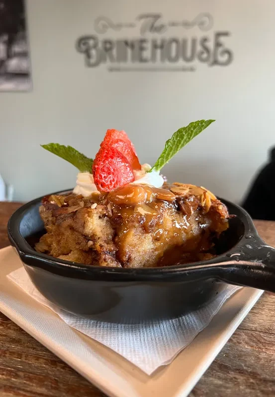 Bread pudding in skillet with caramel, almonds, whipped cream, strawberries, mint.