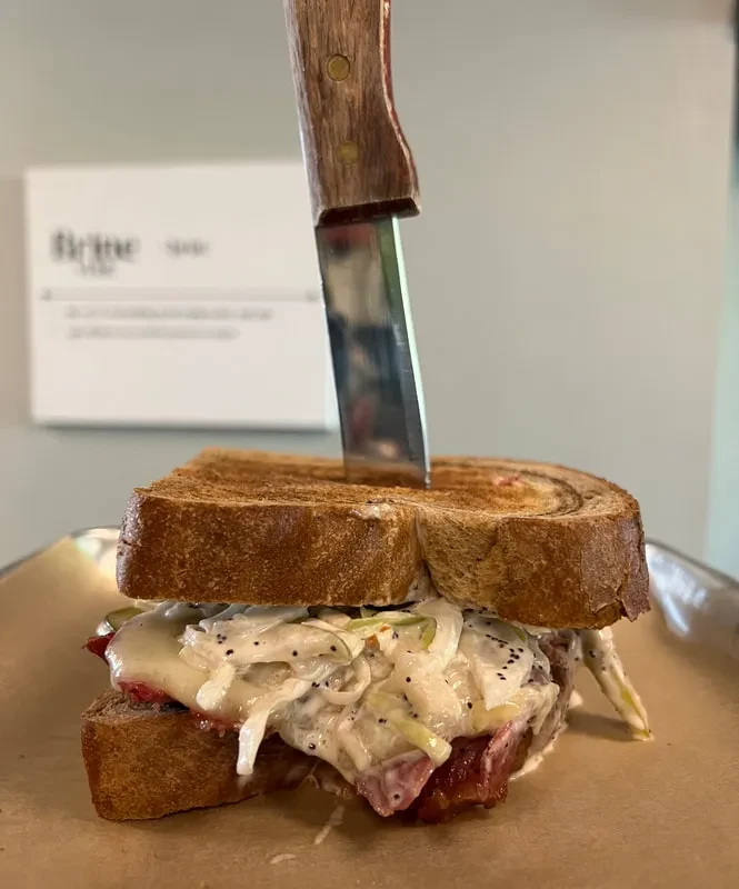 Toasted meat, cheese, and coleslaw sandwich with a knife.