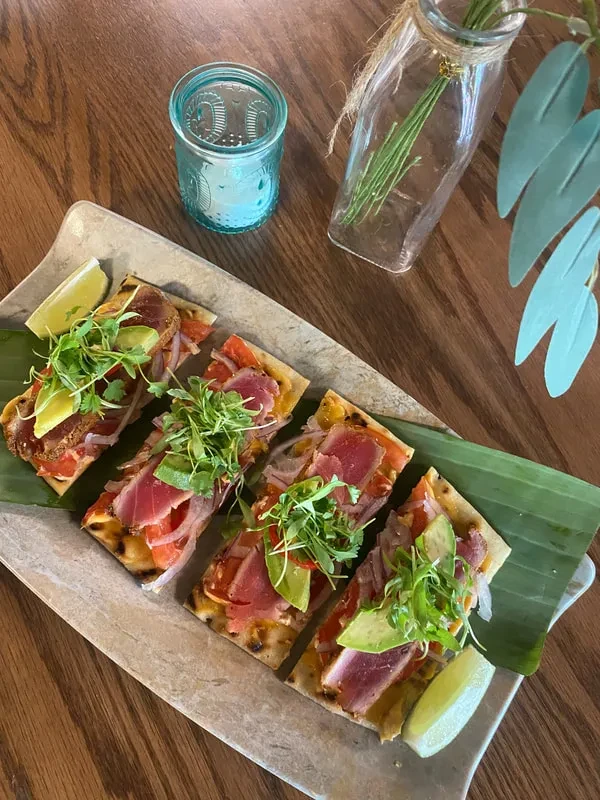 Four seared tuna portions with avocado, microgreens, lime on a platter.