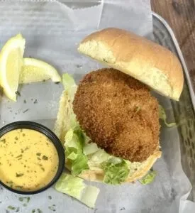 Open-faced fried fish sandwich with lettuce, lemon, and tartar sauce.