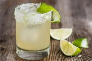 Margarita cocktail with salted rim, lime twist, and ice on wooden surface.