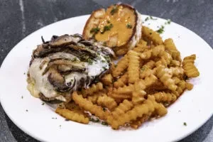 Cheeseburger with mushrooms, crinkle fries, and toasted bread on a white plate.