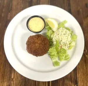 Plate with a fried patty, creamy salad, yellow sauce, and lemon.
