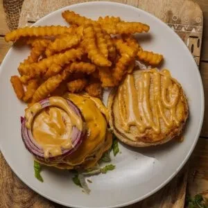 Deconstructed burger with melted cheese, sauce, and crinkle-cut fries.