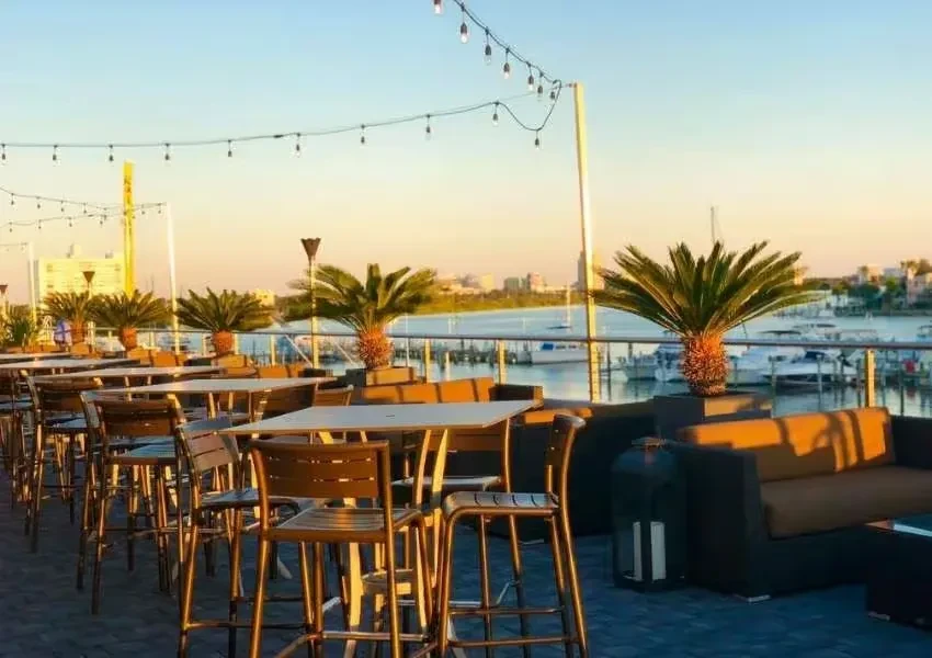 Outdoor dining patio at sunset overlooking a harbor and city.