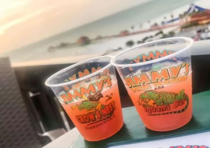 Two branded plastic cups with drinks on a table, waterfront view.