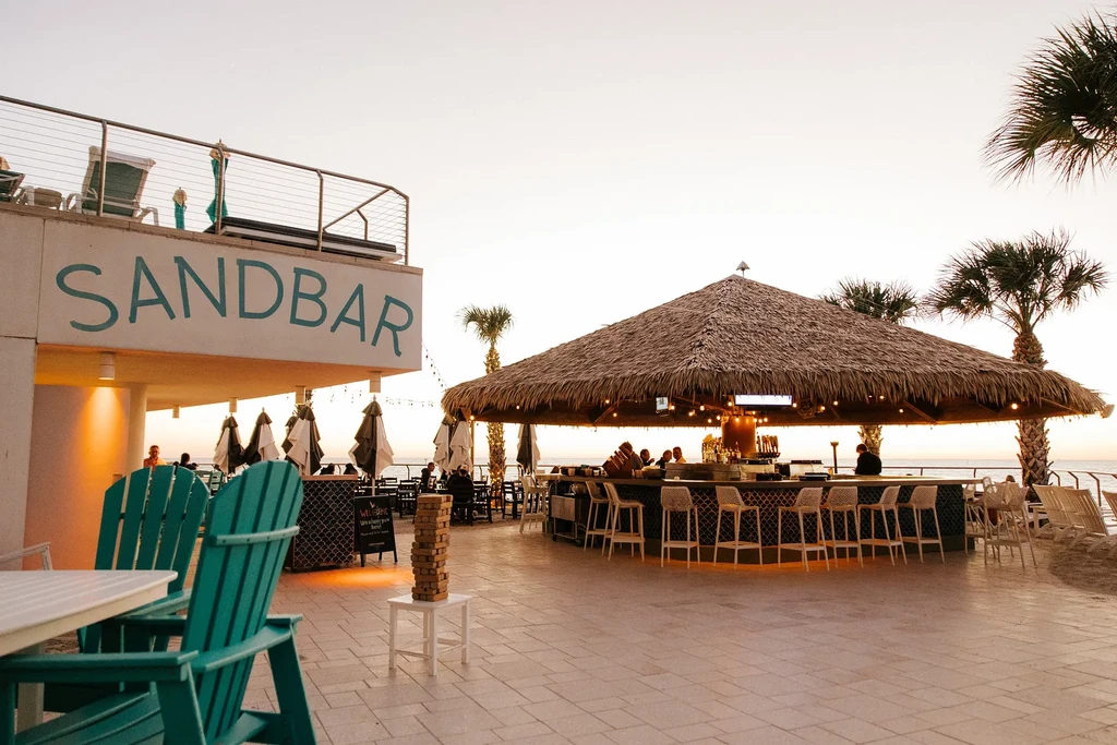 Outdoor Sandbar tiki bar with guests, Adirondack chairs, and ocean view.