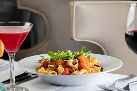 Lobster pasta, red cocktail, and red wine on an elegant dining table.