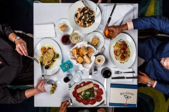 Four people dining at an upscale restaurant table with food and drinks.