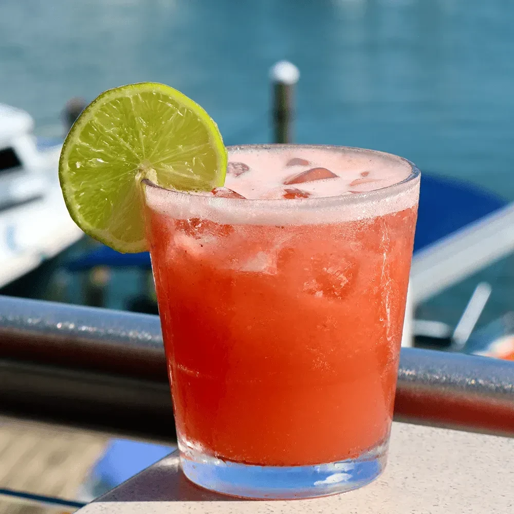 Red-orange iced drink with lime slice, overlooking a marina.