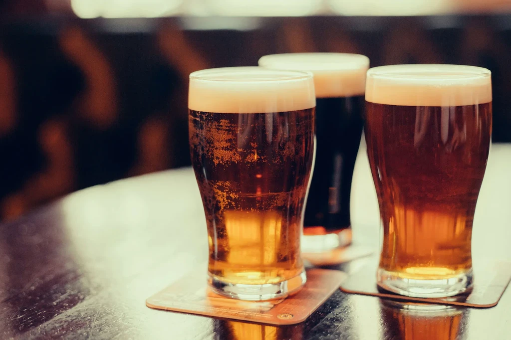 Three beers on a reflective table, two light, one dark.