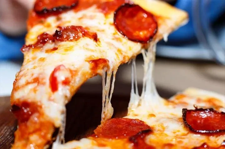 Close-up of a lifted pepperoni pizza slice with stretching melted cheese.