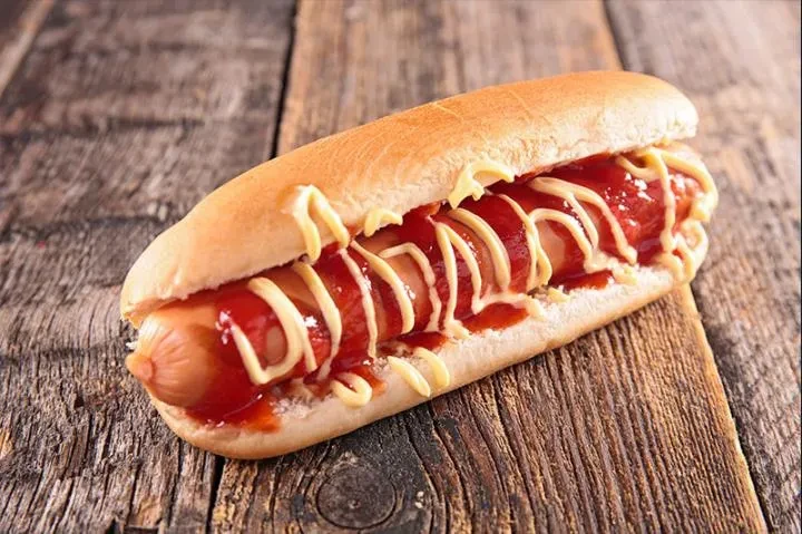 Single hot dog with ketchup and mustard on rustic wood.