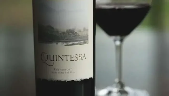 Focused Quintessa red wine bottle and an out-of-focus wine glass.