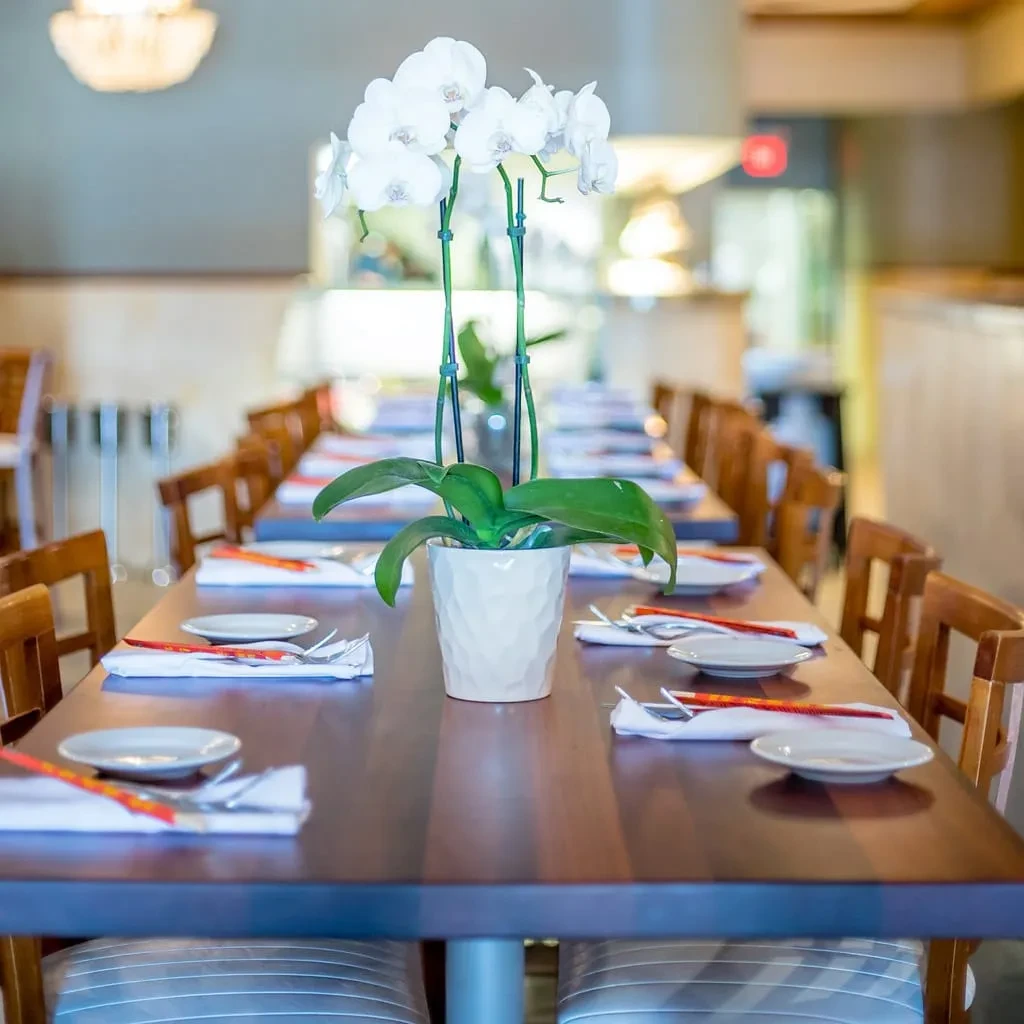 Dark wooden dining table set with white plates, chopsticks, orchid.