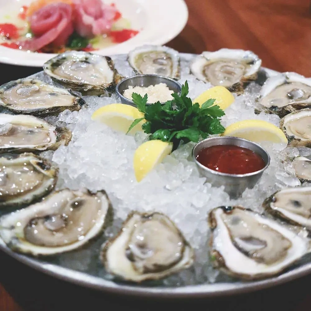 Close-up of fresh oysters on ice with sauces, lemon, and parsley.