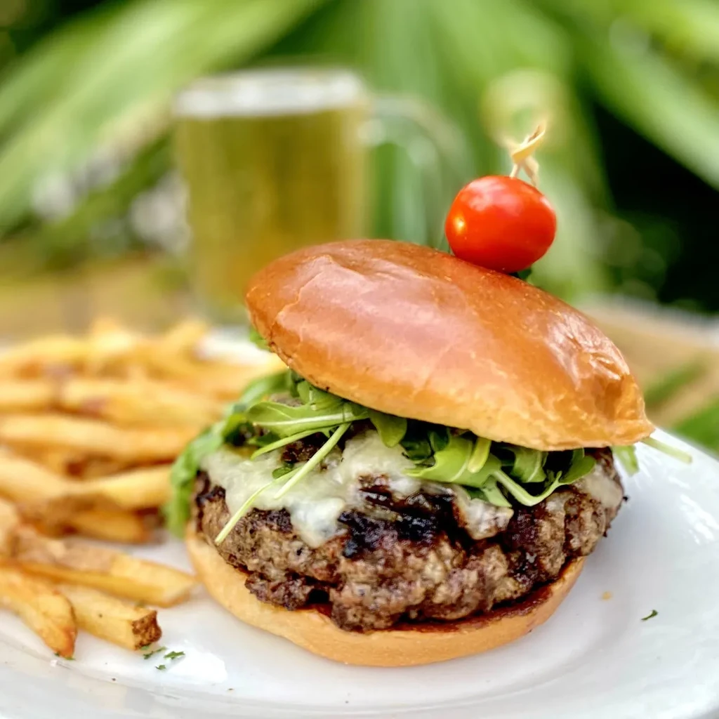 Burger with melted cheese, arugula, tomato skewer, and golden fries.