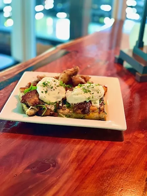 Plated savory breakfast with two poached eggs, crispy meat, and potatoes.