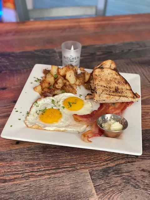 Plated breakfast of fried eggs, crispy bacon, home fries, and toast.