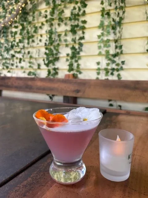 Pink martini cocktail with floral garnish and a flickering candle.
