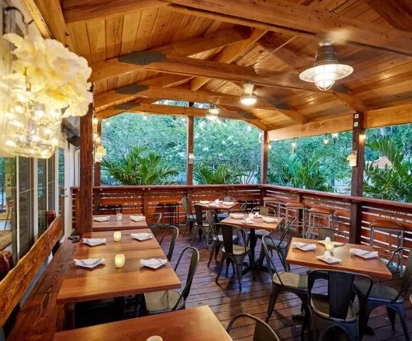 Wooden semi-outdoor restaurant patio with dining tables and lush greenery.