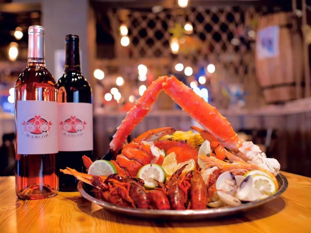 Vibrant seafood platter with crab, shrimp, crawfish, clams, corn, and wine bottles.