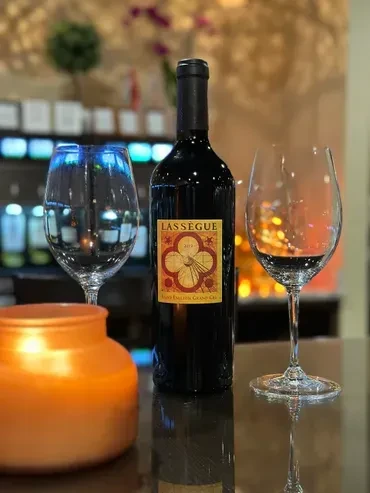LASSÈGUE 2017 red wine bottle, glasses, and candle on bar.